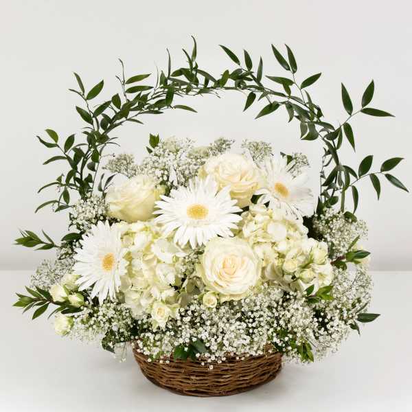 White roses and daisies in a wicker basket with a leafy arch