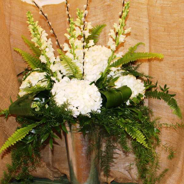 White floral arrangement in a tall glass vase with fern accents