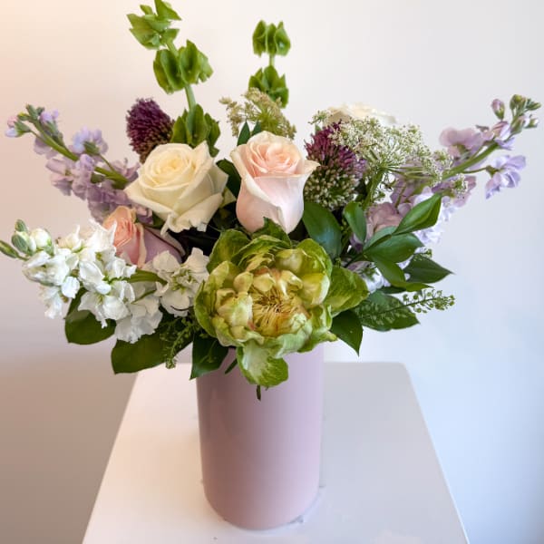 Mixed bouquet of roses, green blooms, and lavender flowers in a pink vase