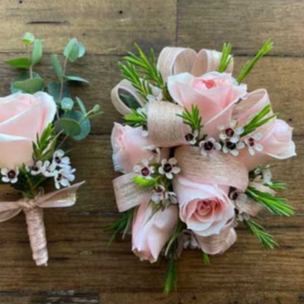 Two pale pink rose boutonnieres with ribbon and small white flowers