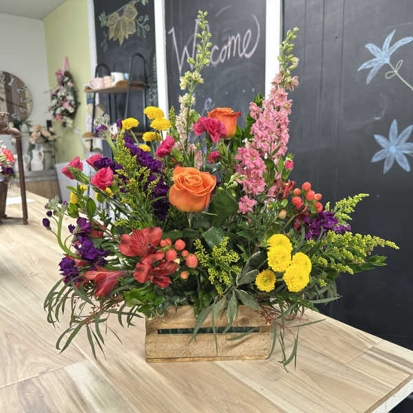 Mixed bouquet in a wooden crate with orange roses and pink, yellow, and purple flowers