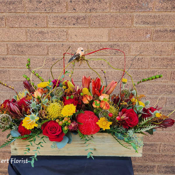 Long floral arrangement in a wooden box with red, yellow, and peach blooms