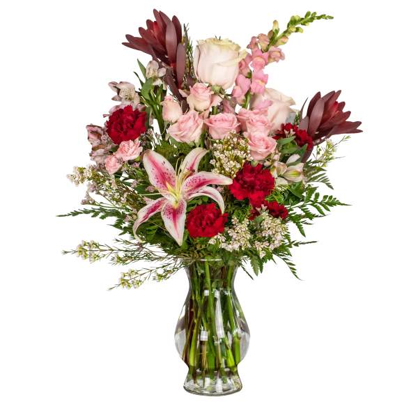 Mixed bouquet of pink roses, red carnations, and a pink lily in a glass vase.