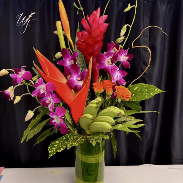 Tropical flower arrangement in a tall glass vase with orchids and orange blooms