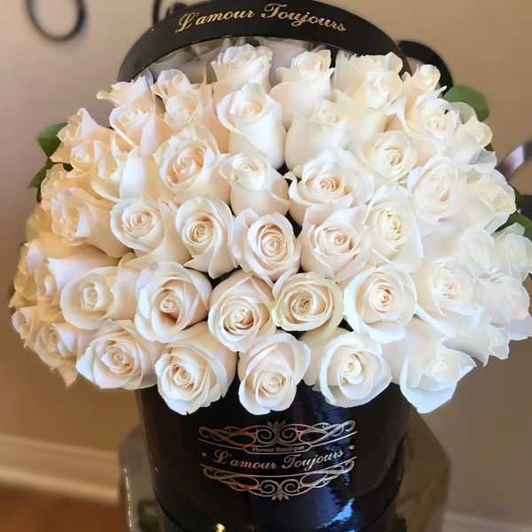 White roses arranged in a black hatbox with gold lettering