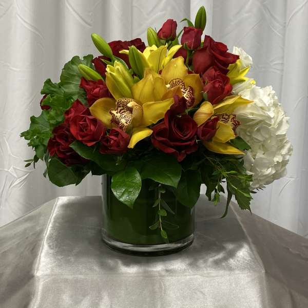 Red roses and yellow orchids in a glass vase with white hydrangea