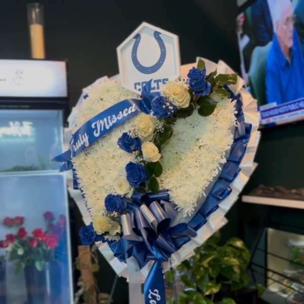 Heart-shaped floral tribute with blue and white roses on a stand