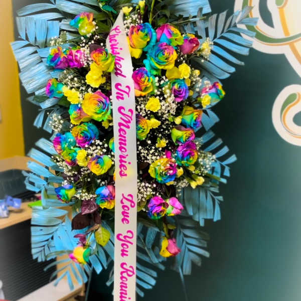 Standing floral tribute with rainbow roses and a memorial ribbon
