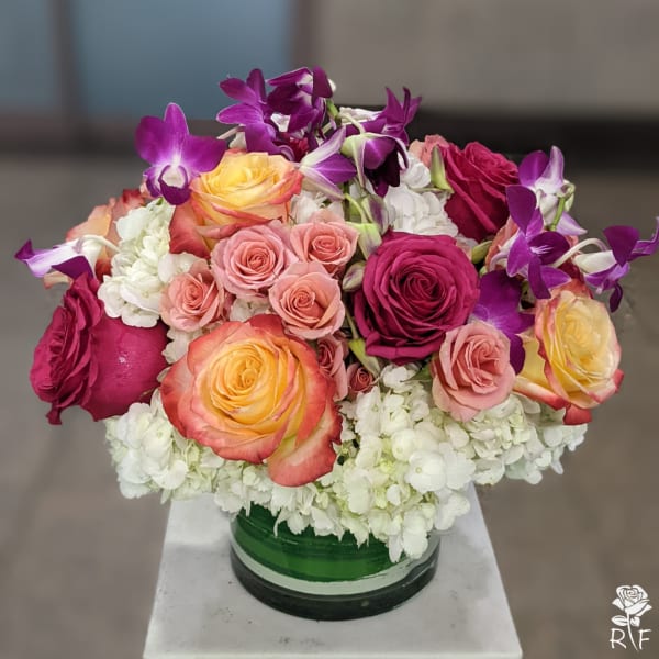 Mixed roses and purple orchids in a green glass vase