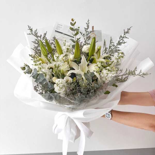 White lily bouquet wrapped in white paper with a ribbon