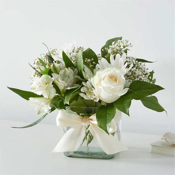 White rose and lily bouquet in a glass vase with a ribbon