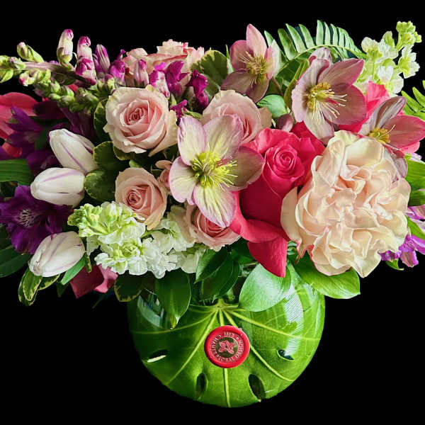 Mixed bouquet of pink roses, tulips, and hellebores in a green vase