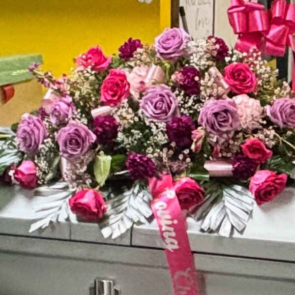 Pink and lavender rose arrangement on a casket with ribbon accents