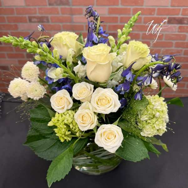Cream roses and blue flowers arranged in a glass vase