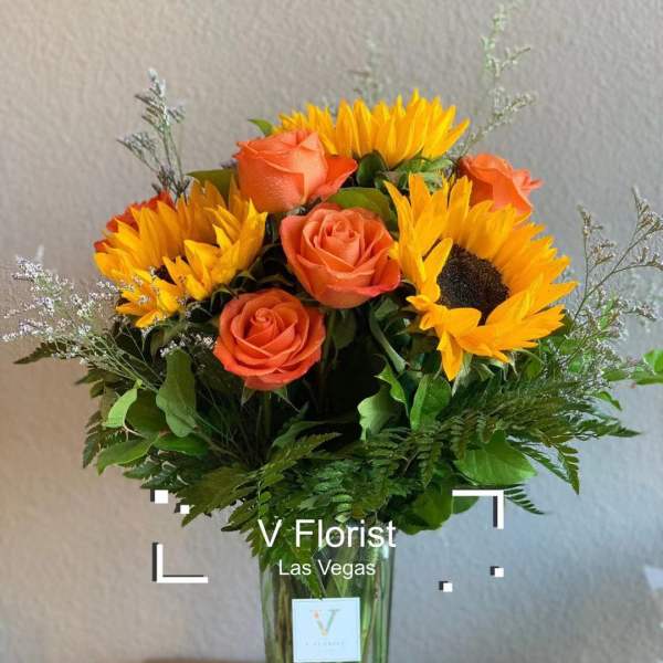 Tall vase of yellow sunflowers and orange roses in a clear glass rectangular vase.