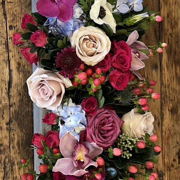 Vertical floral arrangement with roses, orchids, and pale anemones