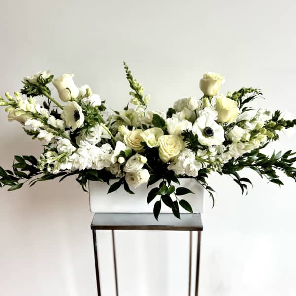 White floral arrangement in a rectangular vase with long greenery