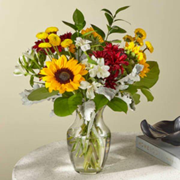 Mixed bouquet with sunflowers, red and yellow blooms in a clear glass vase