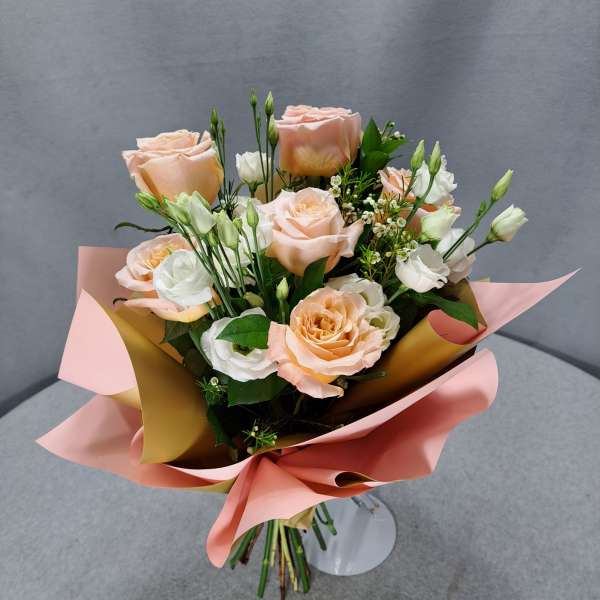 Bouquet of peach and white roses wrapped in pink paper