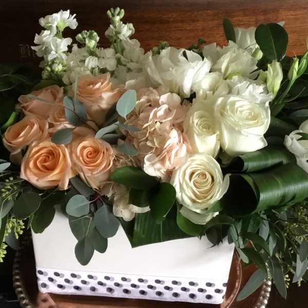 White and peach roses arranged in a white box with greenery