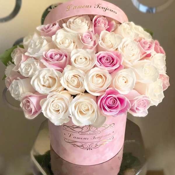 Pink and white roses arranged in a round pink hat box