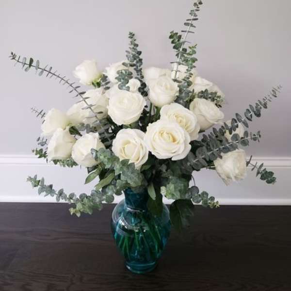 White roses in a blue glass vase with airy eucalyptus stems