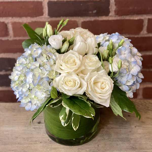 White roses and pale blue hydrangeas in a green glass vase