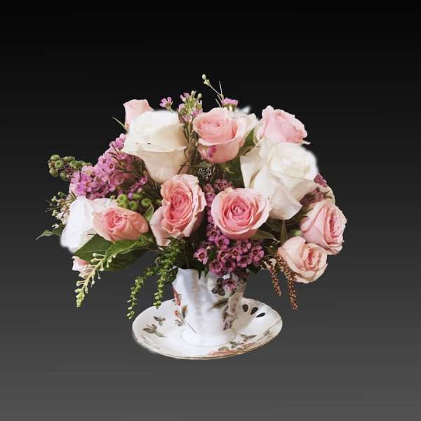 Pink and white roses arranged in a teacup on a saucer