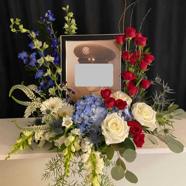 Floral tribute around a framed portrait with red and white roses and blue flowers