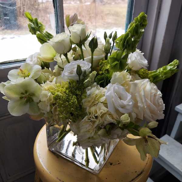 White floral arrangement in a square glass vase with green accents