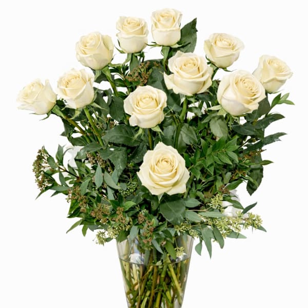 White roses arranged in a clear glass vase with greenery