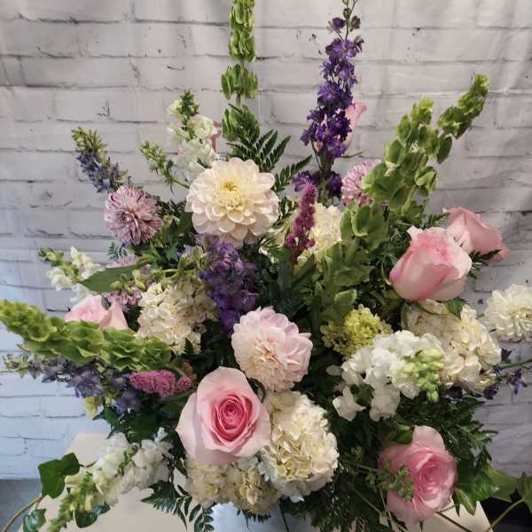 Tall pastel floral arrangement with pink roses, white blooms, and purple flowers in a white vase