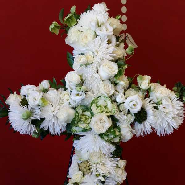 White floral cross on a stand against a red background