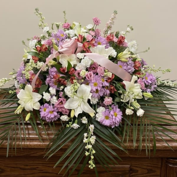 Large pastel floral arrangement with lilies, daisies, and a pink ribbon