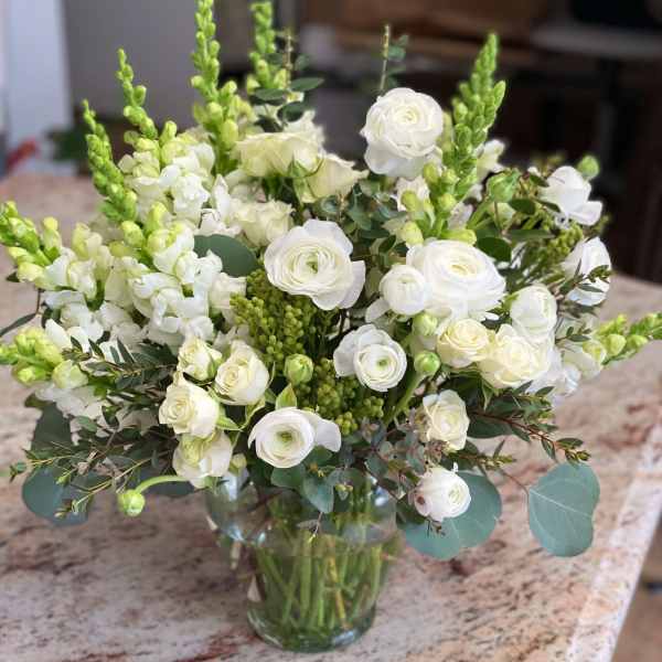 White flowers and green spikes arranged in a clear glass vase