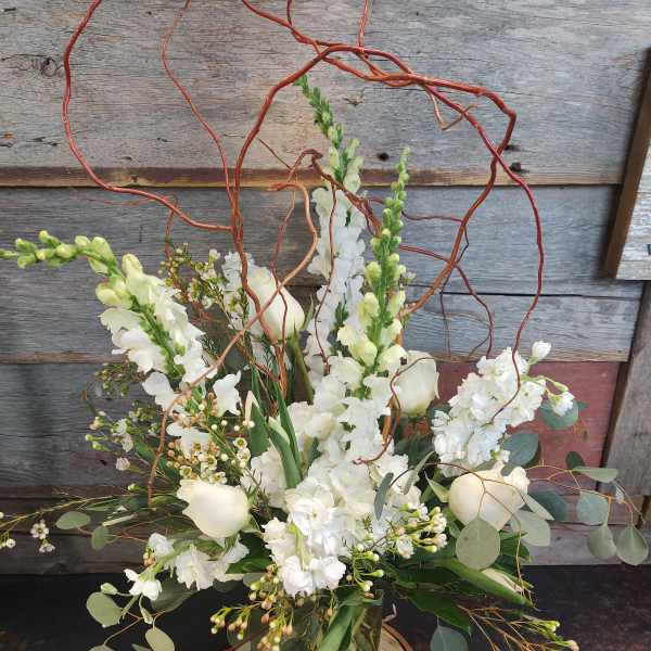 White floral arrangement in a glass vase with curly branches