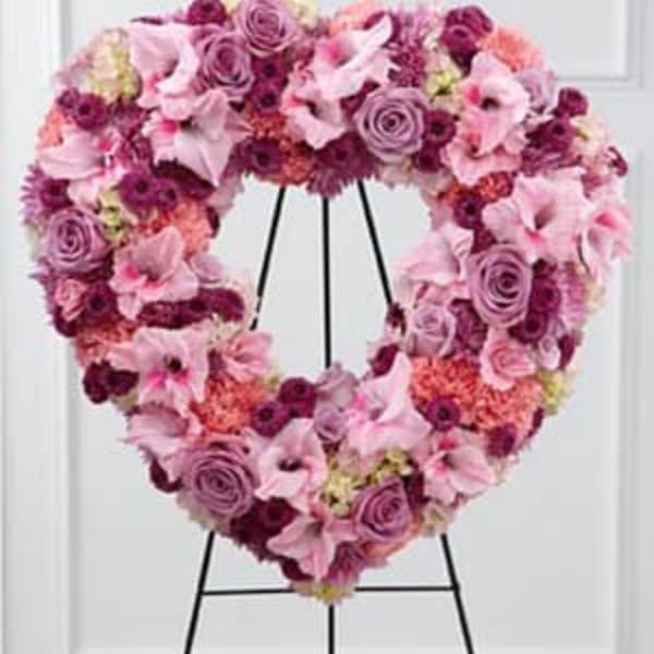 Heart-shaped floral wreath on a black stand with pink and purple blooms