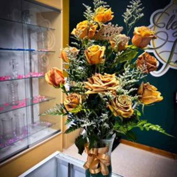 Tall bouquet of orange roses in a gold vase with a ribbon