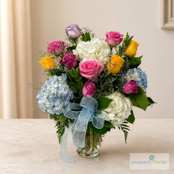 Mixed bouquet of roses and hydrangeas in a glass vase with a blue ribbon