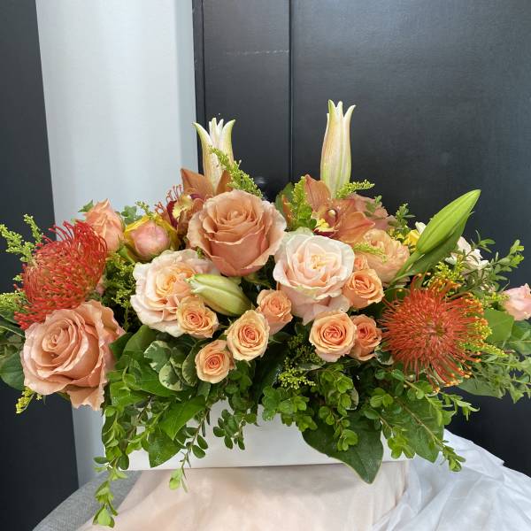 Peach roses and orange pincushion blooms in a white rectangular vase