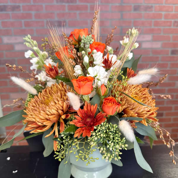 Orange roses and chrysanthemums in a white vase with dried accents