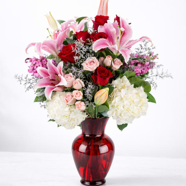 Bouquet of pink lilies, red roses, and white hydrangeas in a red glass vase