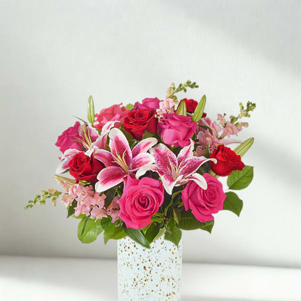 Pink and red roses with lilies in a speckled white vase
