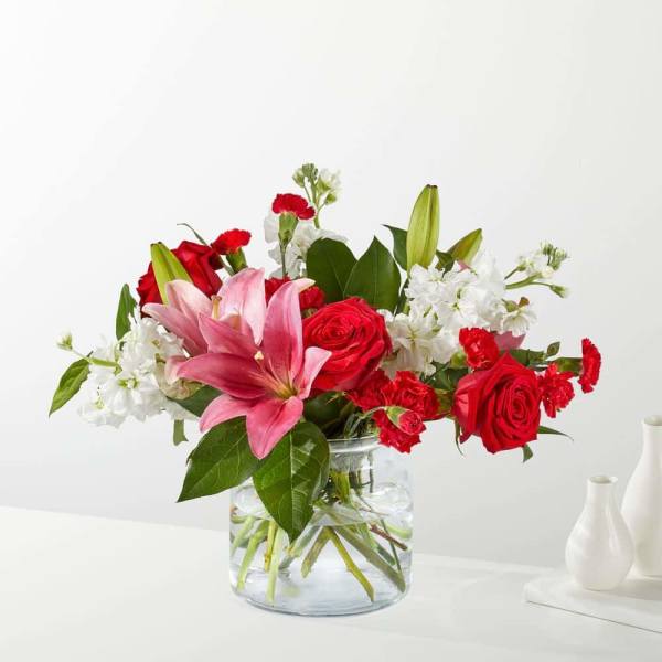 Bouquet of red roses, pink lilies, and white flowers in a clear glass vase