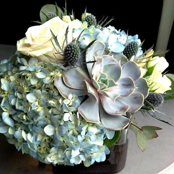 Bouquet of pale blue hydrangeas, white roses, and succulents in a vase