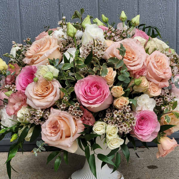 Low pedestal arrangement of peach and pink roses with white accents in a white compote vase