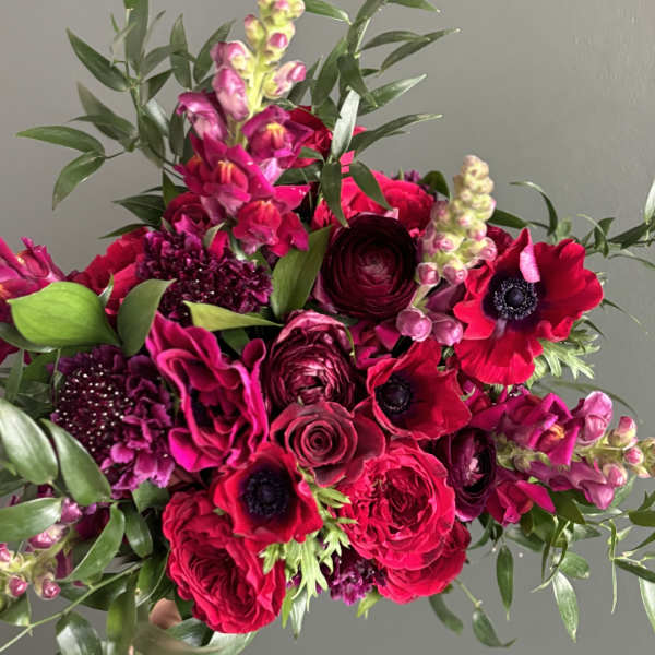 Handheld bouquet of hot pink and burgundy flowers with greenery