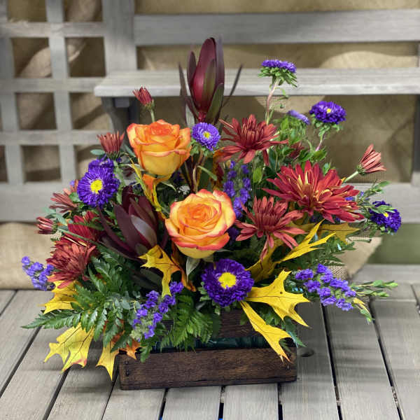 Autumn floral arrangement with orange roses and purple daisies in a wooden box