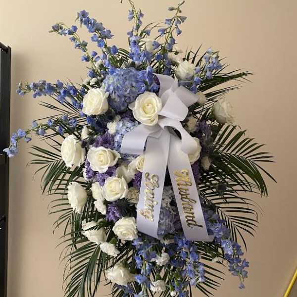 Standing floral spray with white roses, blue flowers, and a white ribbon