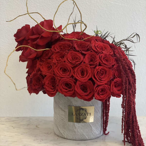 Red rose arrangement in a gray cylindrical box with trailing burgundy accents